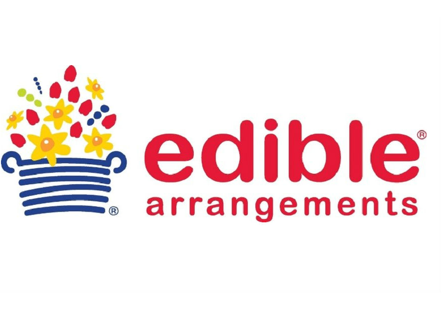This is the Edible Arrangements logo. It has a clip-art blue basket, with clip-art pineapple Daisies, red strawberries, green grape squares, and blueberry squares in the basket. To the right of the baskets, there is an edible arrangements text in red 